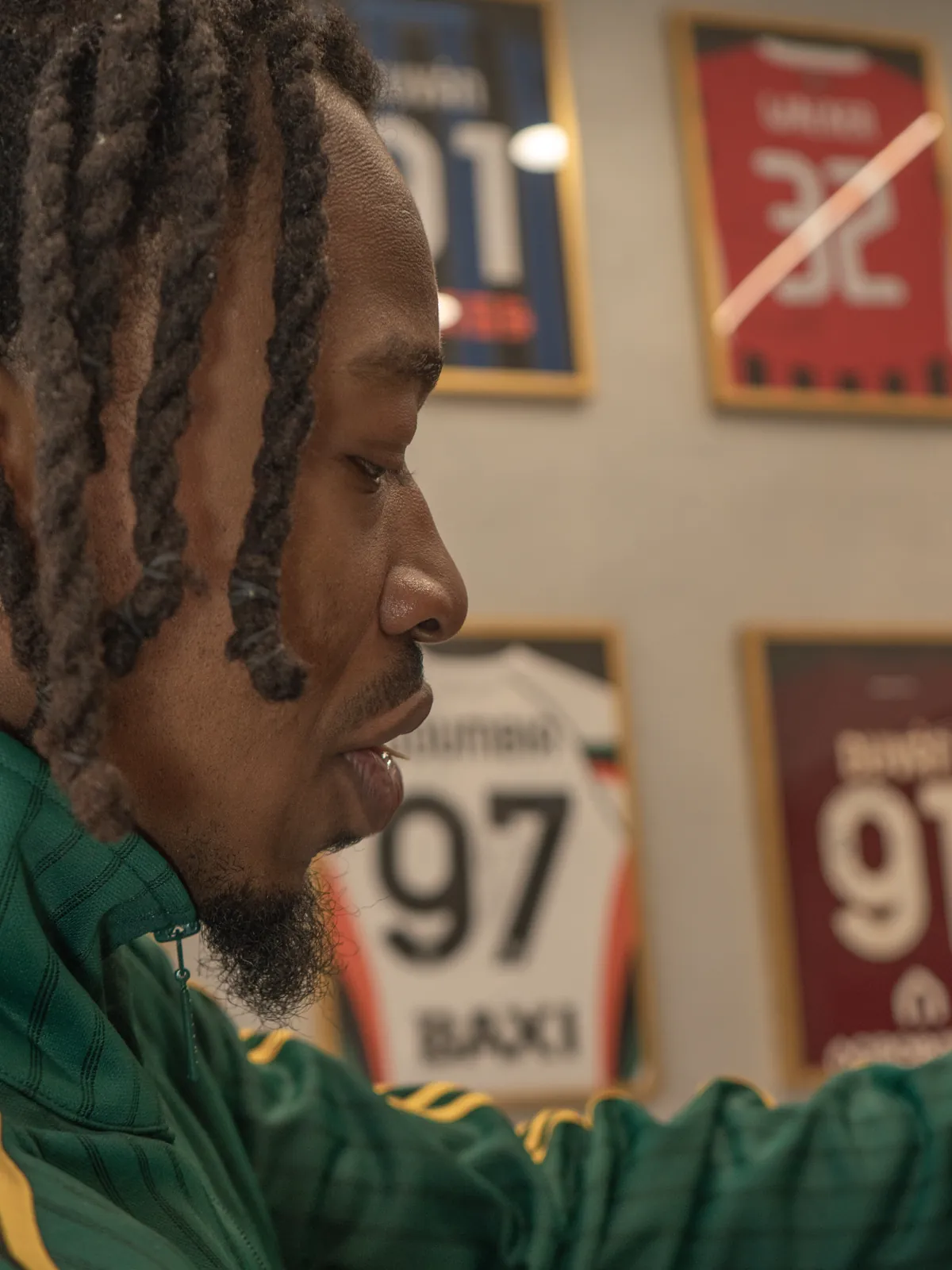 Hermann in profile, focused, with the signed shirts behind him
